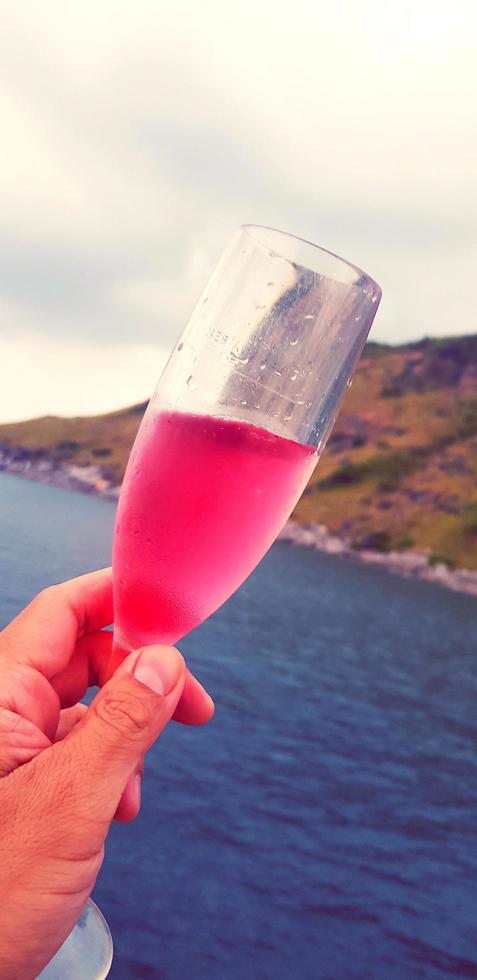 mão do homem segurando o copo de vinho tinto com fundo de mar, montanha e céu em tom vintage. celebrar e festejar o conceito entre a natureza e as viagens. foto