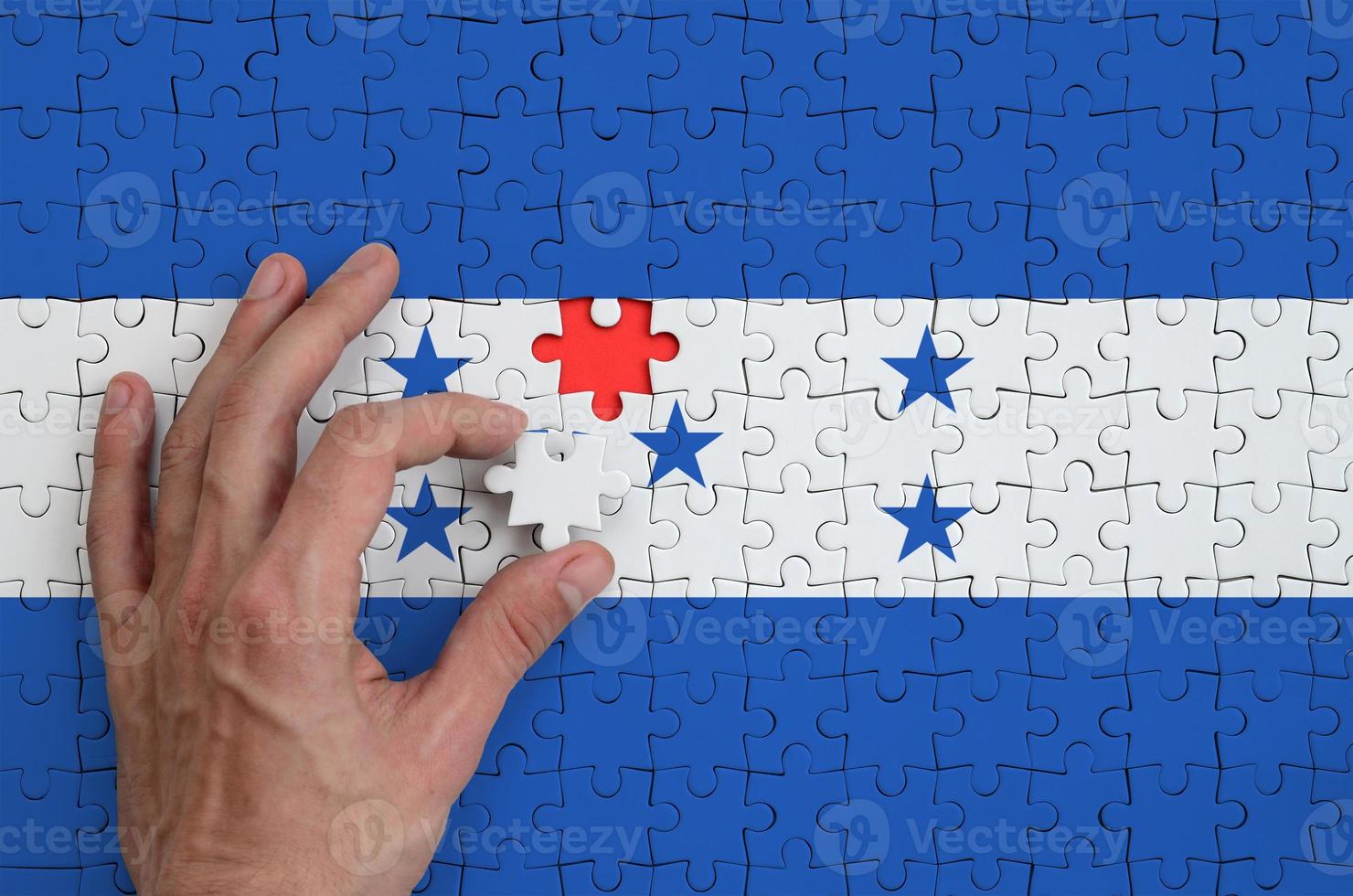 a bandeira de honduras é retratada em um quebra-cabeça, que a mão do homem completa para dobrar foto