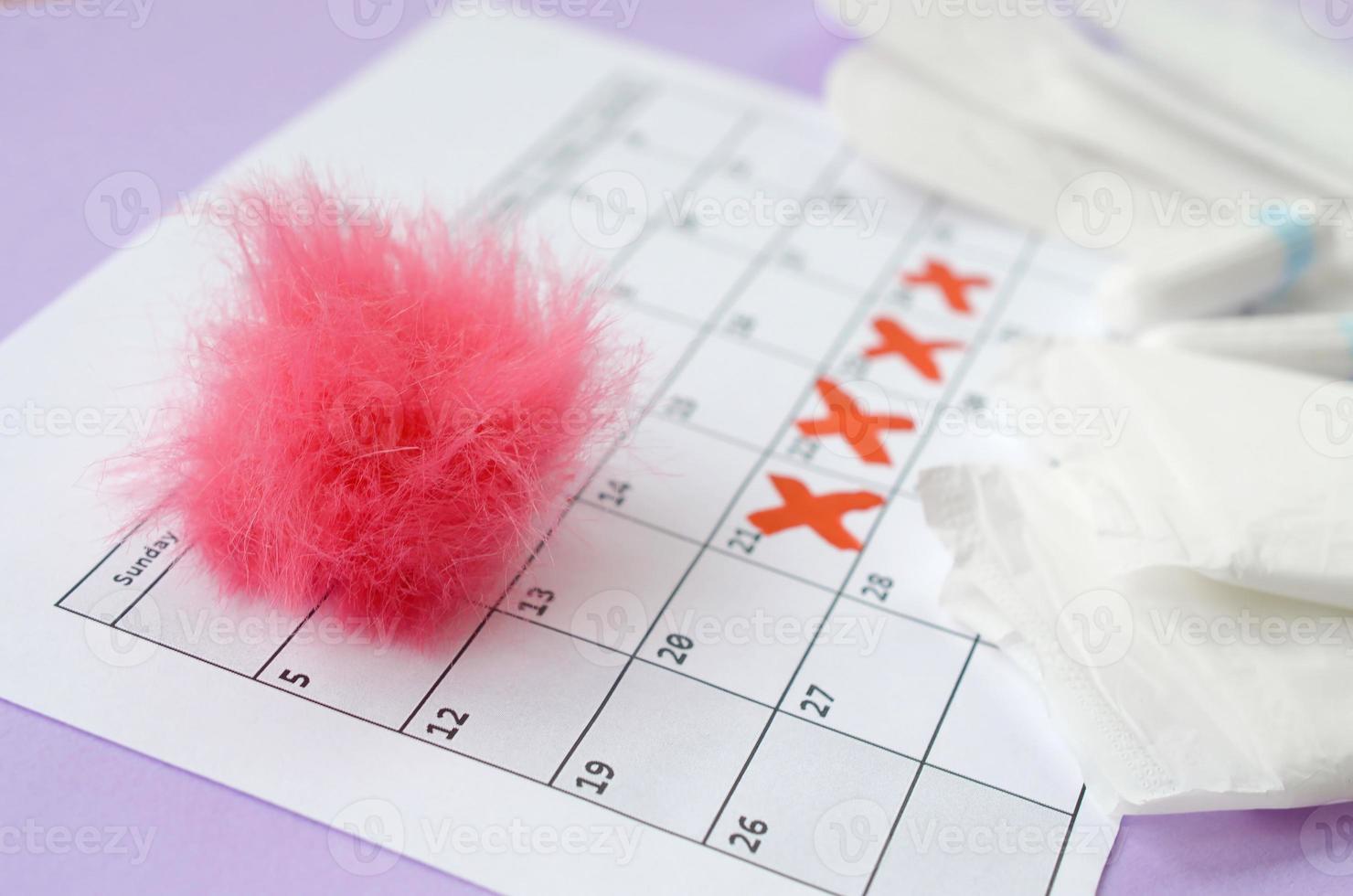 almofadas menstruais e tampões no calendário do período de menstruação com marcas da cruz vermelha encontra-se no fundo lilás foto