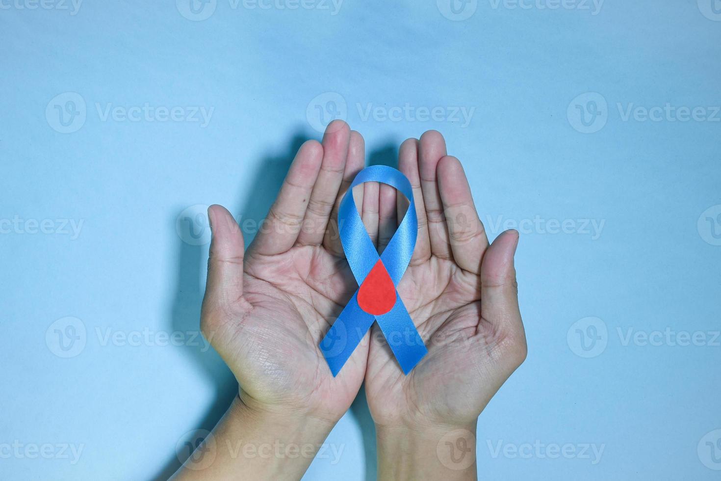 vista superior consciência de fita azul com gota de sangue vermelho nas mãos do homem isoladas em um fundo azul. 14 de novembro, dia mundial do diabetes. copyspace foto