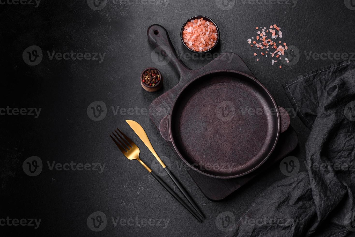 panela vazia de ferro marrom com utensílios de cozinha em um fundo escuro de concreto foto