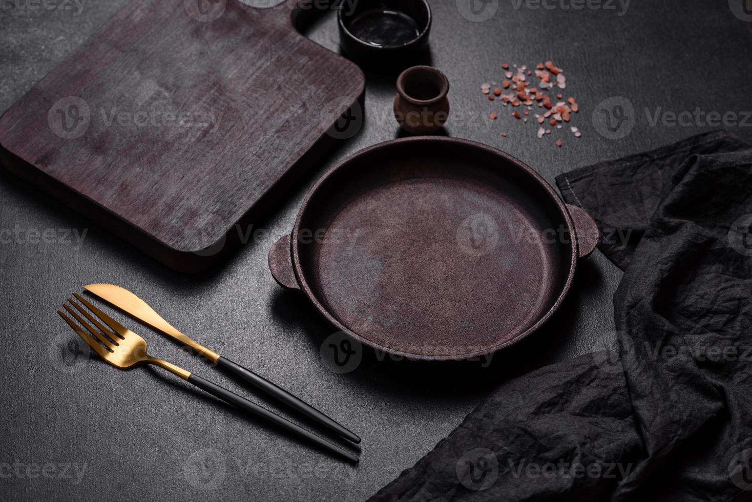 panela vazia de ferro marrom com utensílios de cozinha em um fundo escuro de concreto foto