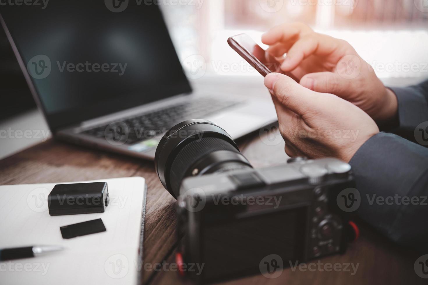 um homem olha a foto no smartphone a partir de dados de transferência com câmera, verificação de trabalho de fotografia e equipamento de fotografia na mesa