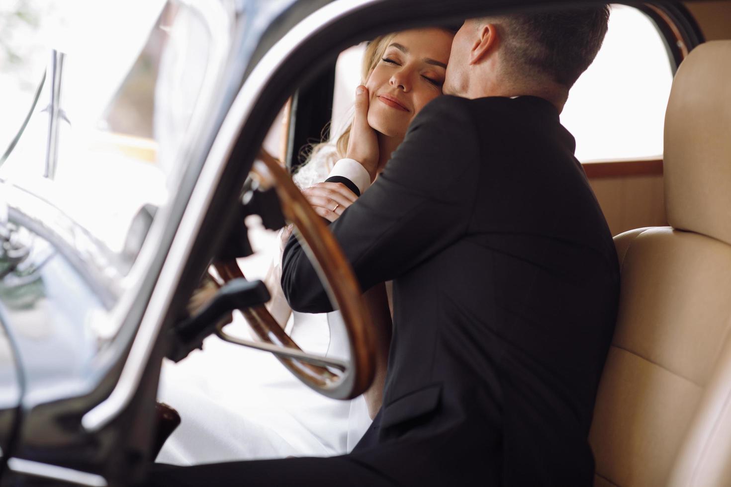 casal de noivos elegantes se abraçando em um carro retrô foto