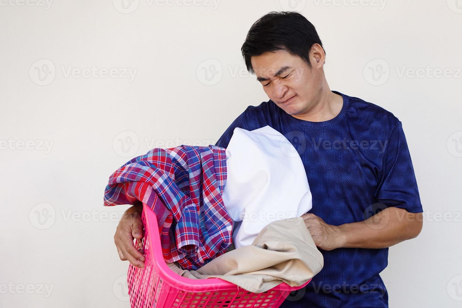 homem asiático segura cesto de roupas, sente-se entediado e preguiçoso, não quer lavar roupa. conceito, tarefa chata, tarefas domésticas. homem não quer lavar roupa. foto