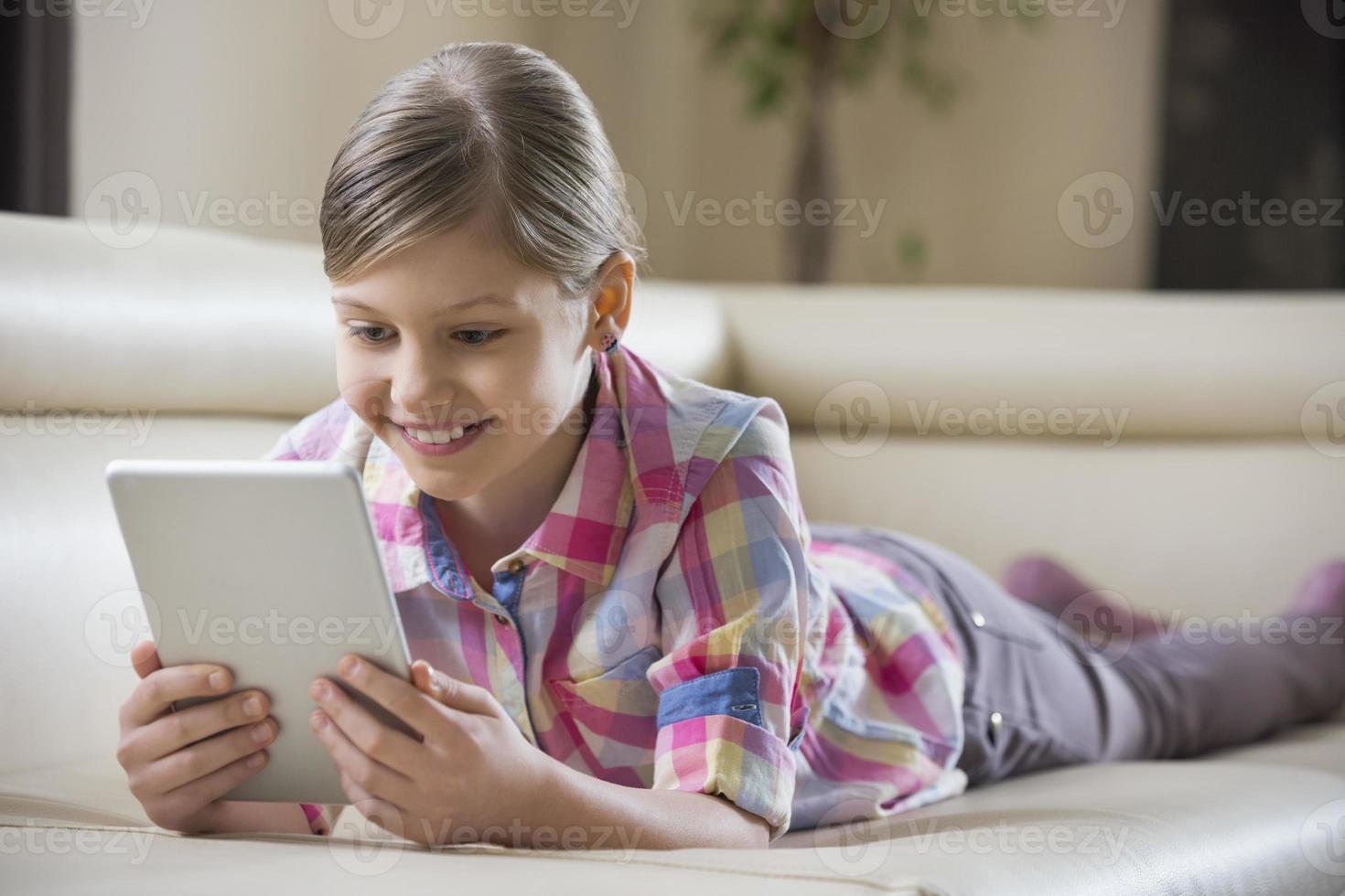 garota sorridente usando tablet pc enquanto estava deitada no sofá foto