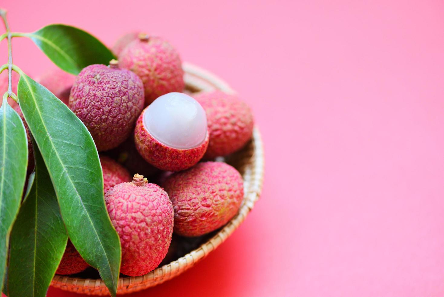 fatia de lichia descascada em fundo rosa vermelho - lichia fresca com folhas verdes colhidas na cesta do verão de frutas tropicais na tailândia foto