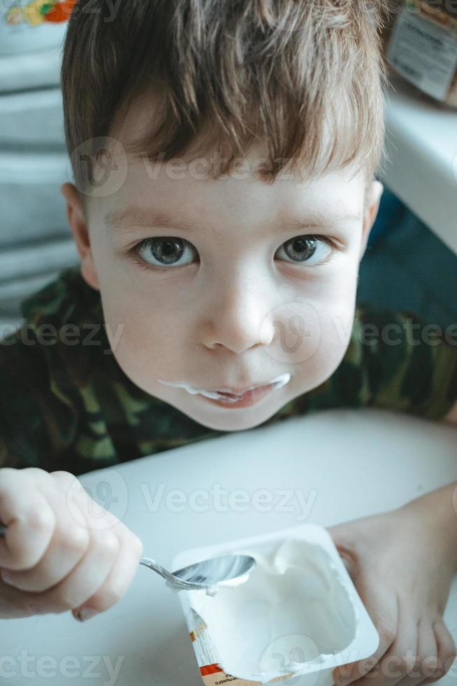 menino bonitinho com olhos grandes come iogurte com uma colher foto