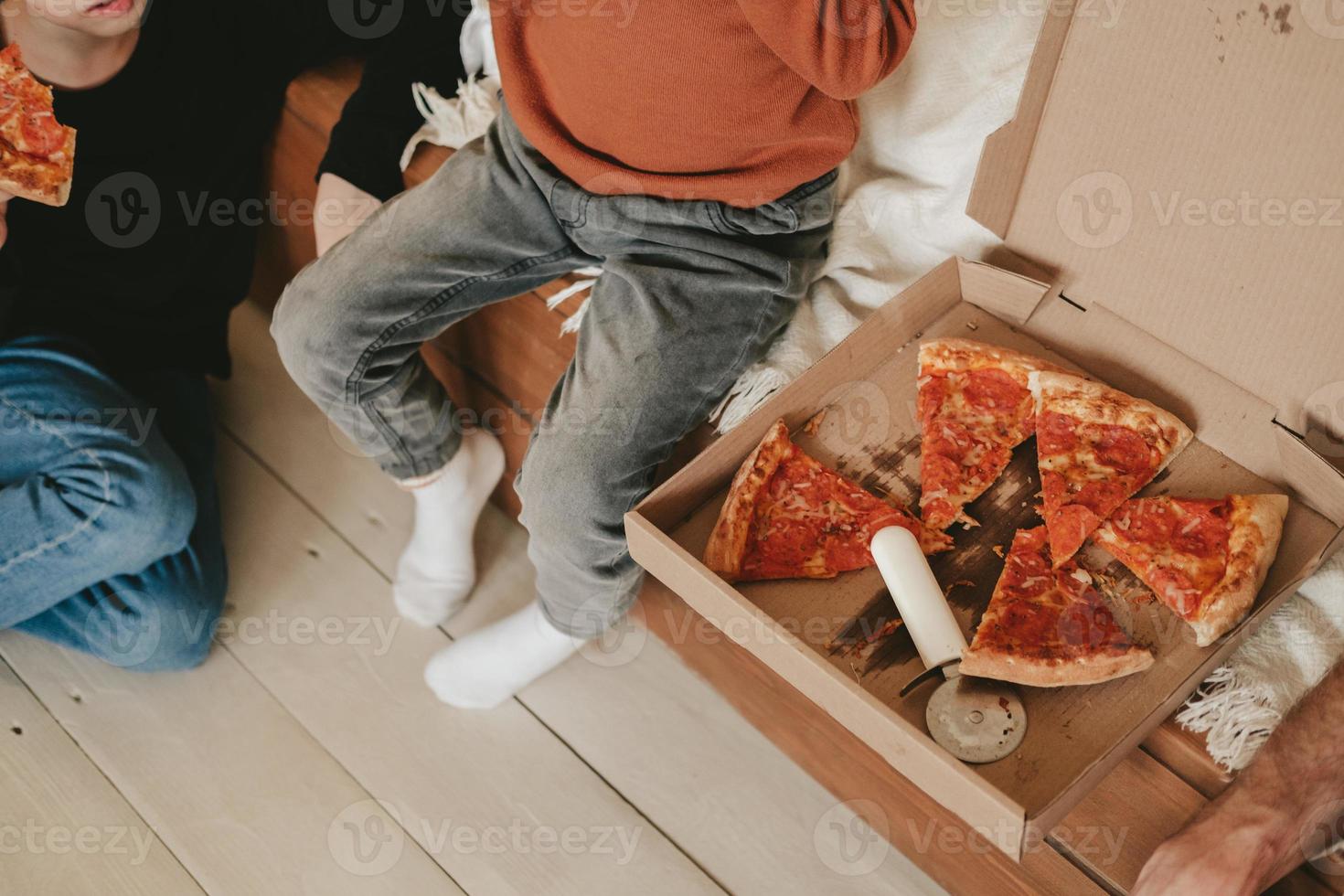 lanche na pizza de pepperoni, fora da caixa no chão, vista de cima. caixa de pizza e faca redonda com fatias de pizza na caixa. entrega de comida em casa foto