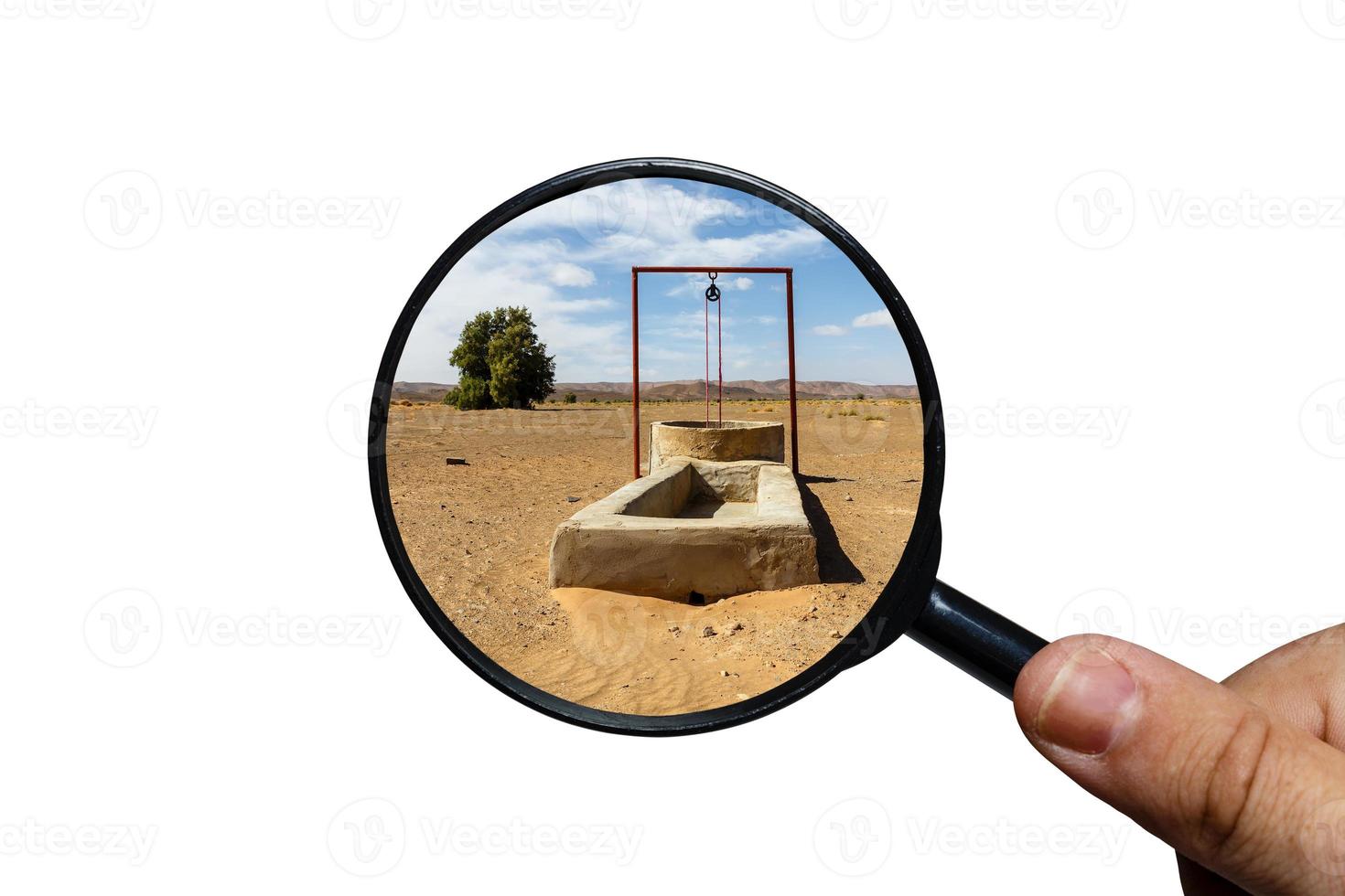 água bem no deserto do saara, vista através de uma lupa sobre um fundo branco, lupa na mão foto