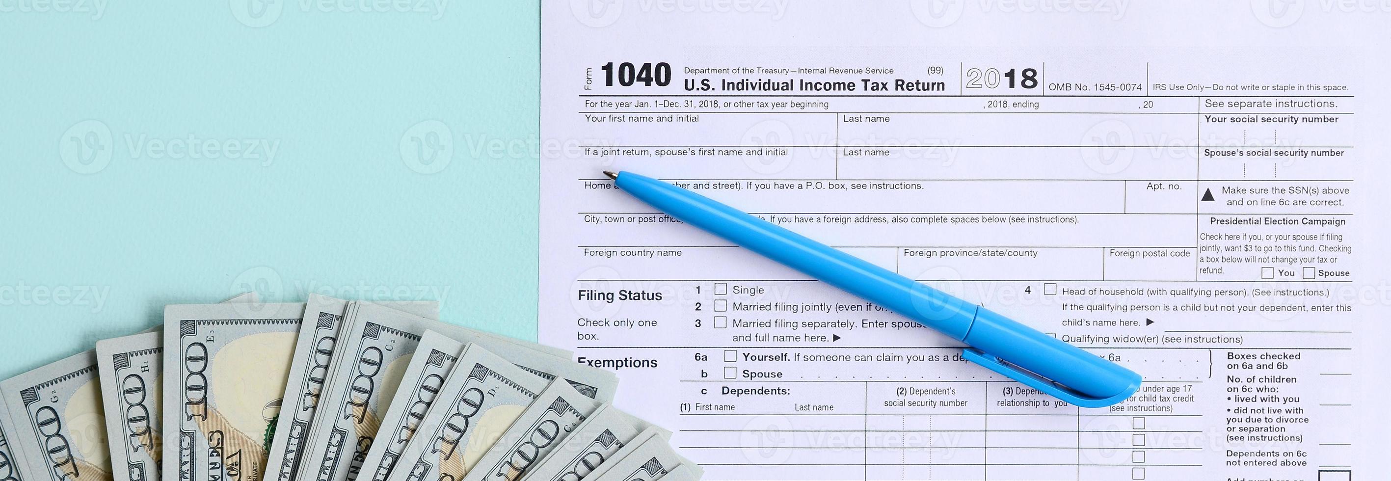 1040 formulário de imposto fica perto de notas de cem dólares e caneta azul sobre um fundo azul claro. nos declaração de imposto de renda pessoa física foto