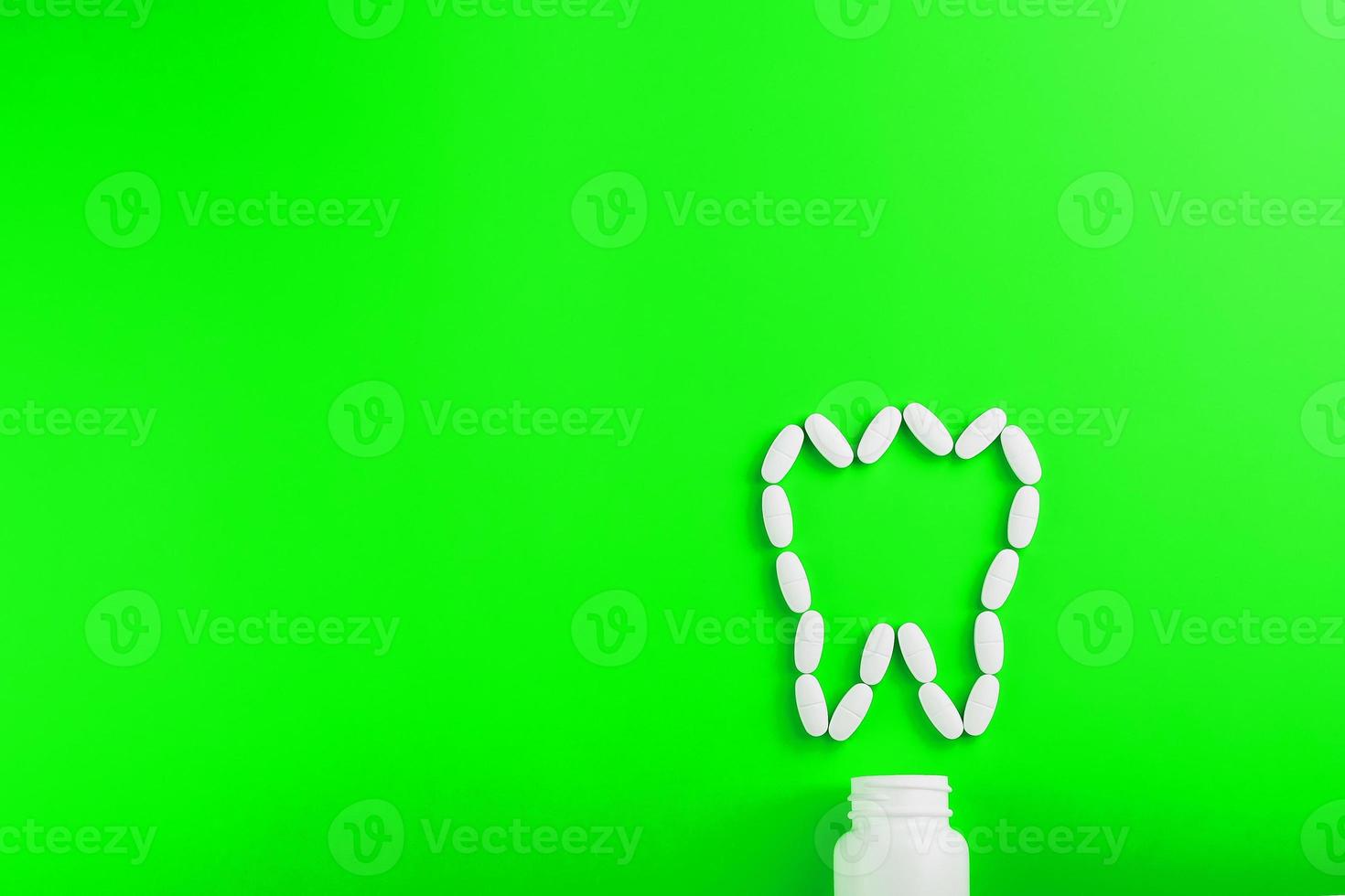 vitamina de cálcio na forma de um dente derramado de uma jarra branca sobre um fundo verde. foto