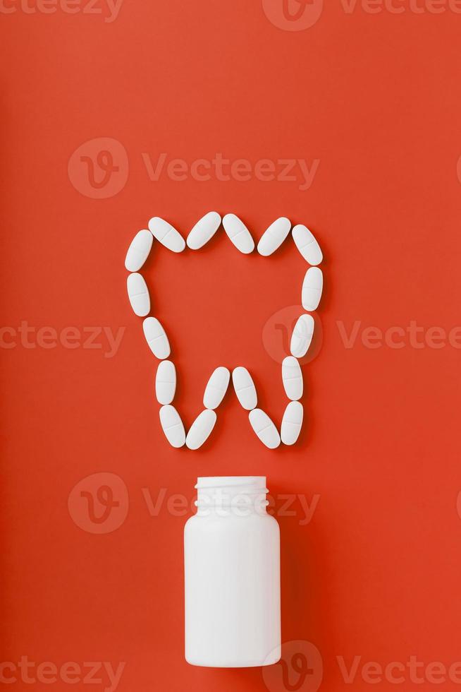 vitamina de cálcio na forma de um dente derramado de uma jarra branca sobre fundo vermelho. foto