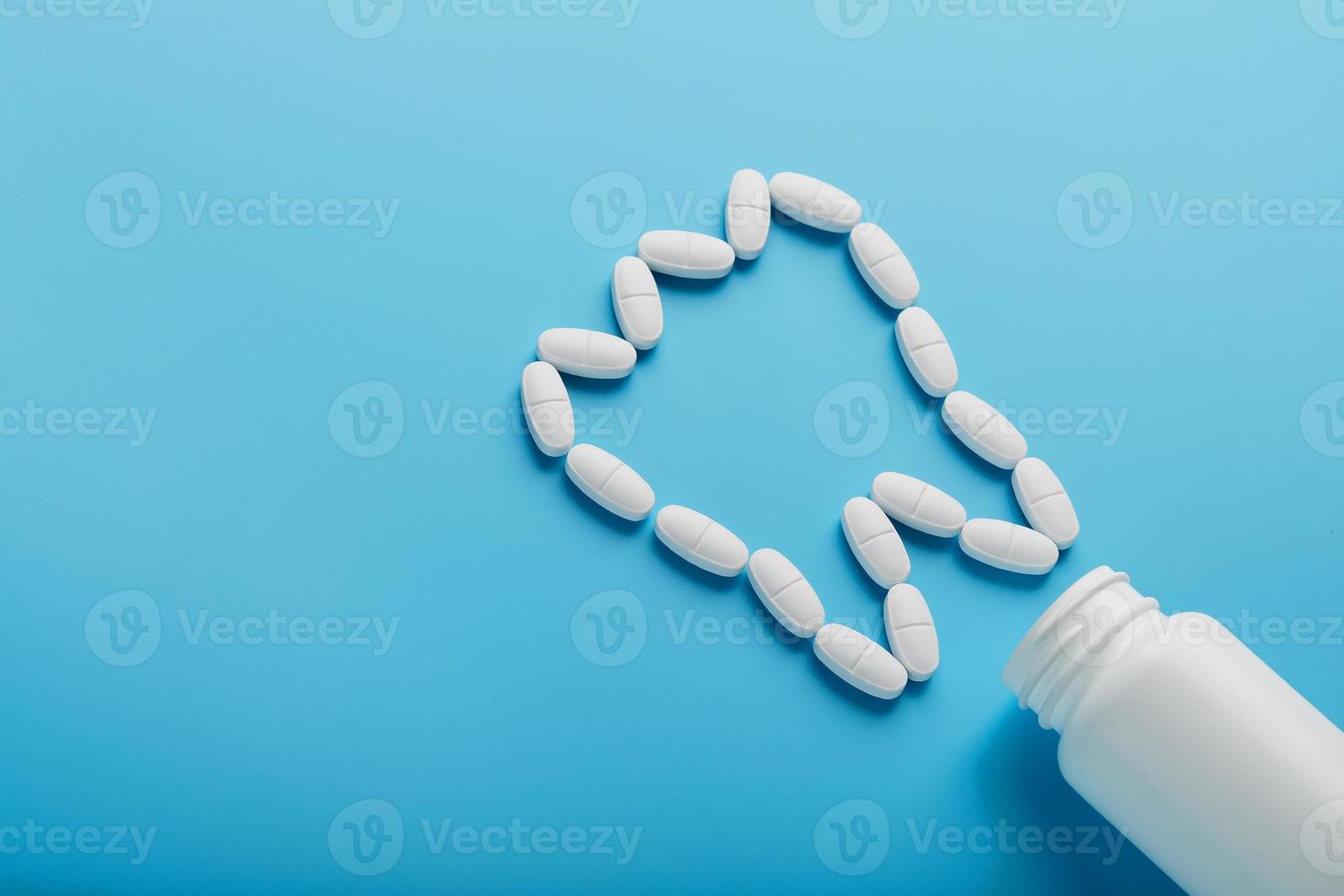 vitaminas brancas com cálcio ca, d3 na forma de um dente espalhado de uma jarra branca sobre fundo azul foto
