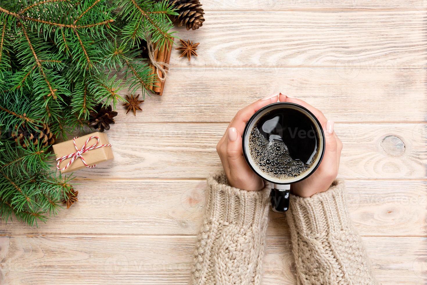 mãos femininas segurando uma xícara de café na mesa de madeira com decoração de natal. vista superior com espaço de cópia foto