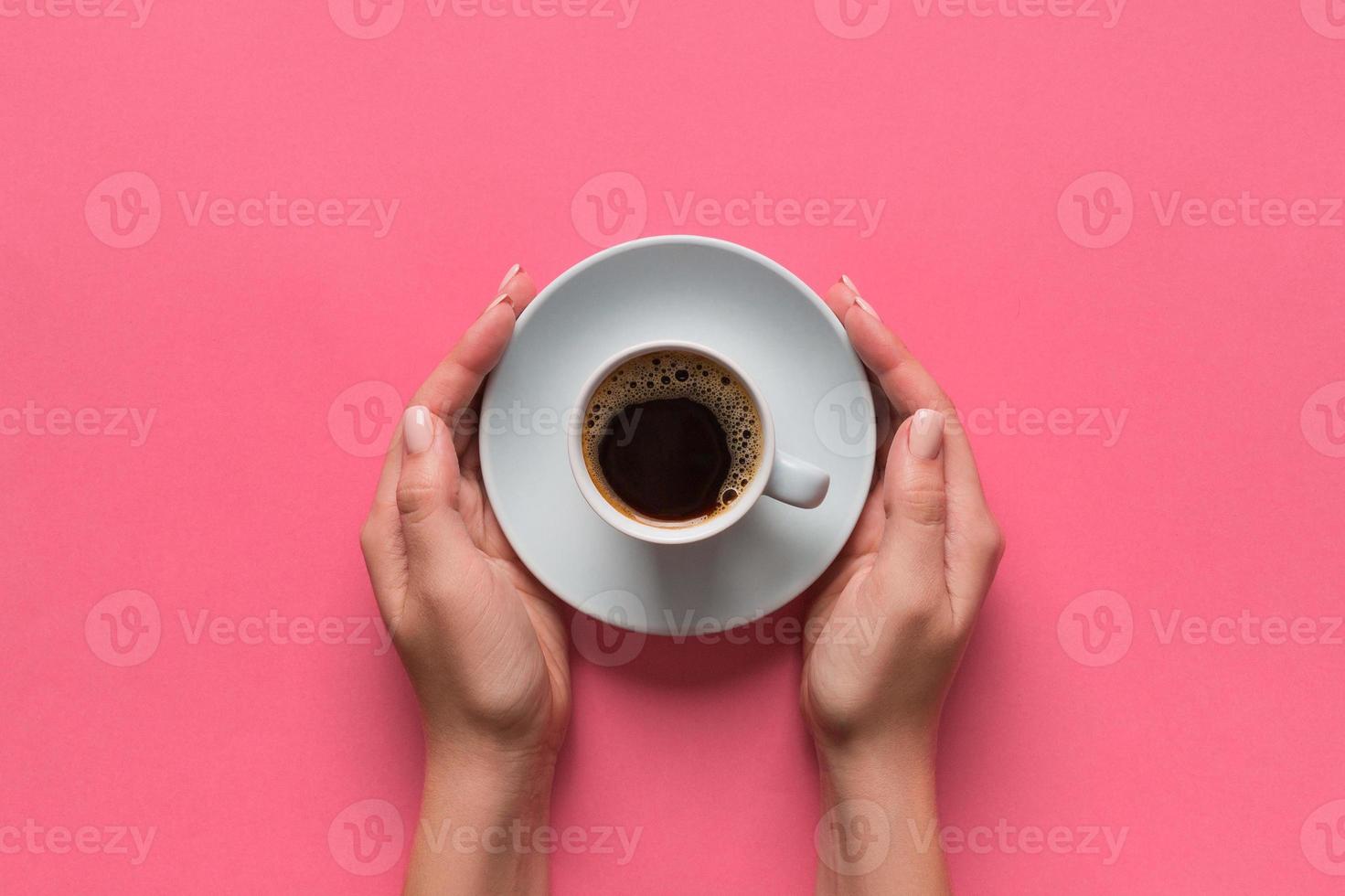 alto ângulo de mãos de mulher segurando uma xícara de café no estilo minimalista de fundo rosa. configuração plana, vista superior isolada foto