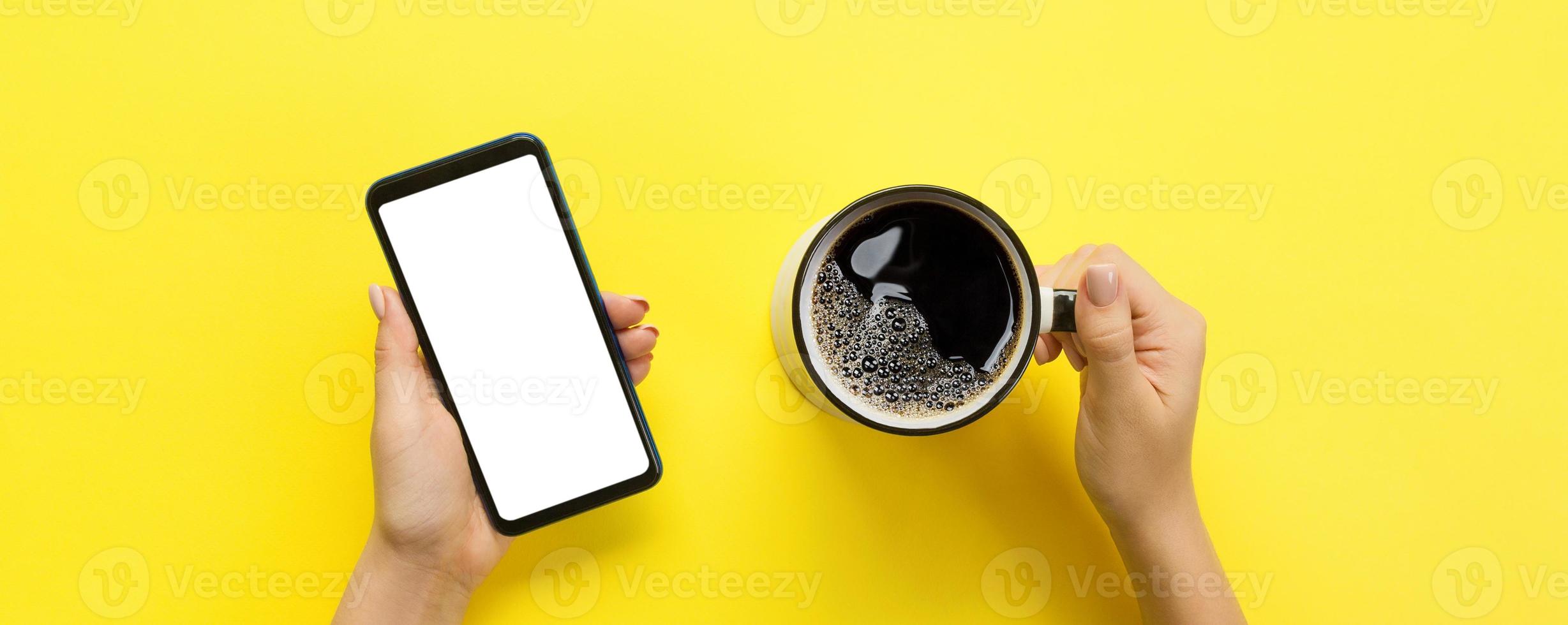 mãos femininas segurando um celular preto com tela branca em branco e caneca de café. imagem de maquete com espaço de cópia para você projetar. banner de vista superior em fundo amarelo, configuração plana foto