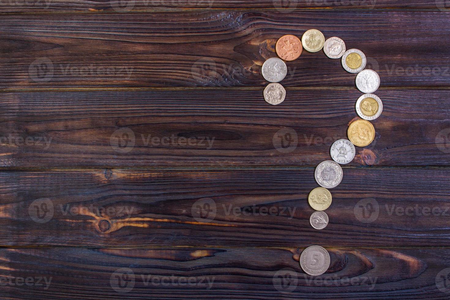 ponto de interrogação de moedas de diferentes países em um fundo de madeira foto