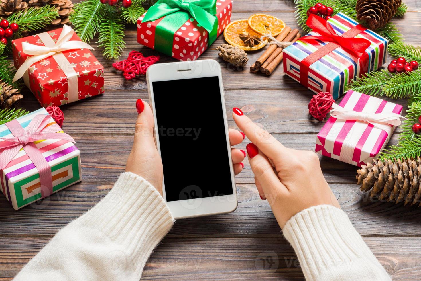 vista superior de uma mulher segurando um telefone na mão no fundo de madeira do ano novo feito de abeto e decorações festivas. conceito de férias de natal. brincar foto