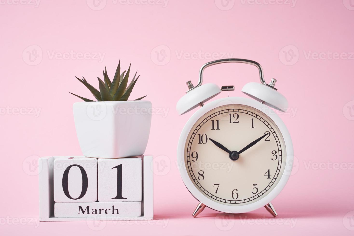 despertador e blocos de calendário de madeira com data 1 de março no fundo rosa. foto