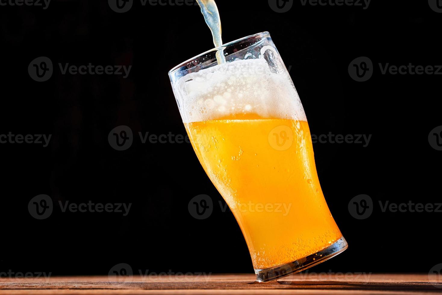 cerveja derramando em um copo no fundo escuro foto