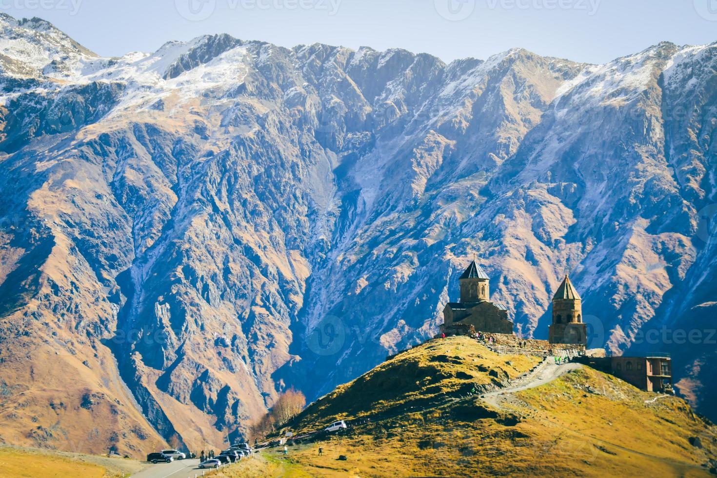 stepantsminda, gergeti, georgia. famosa igreja gergeti trinity tsminda sameba na paisagem do início do inverno. SUV se movendo perto da igreja na bela paisagem georgiana no início do inverno foto