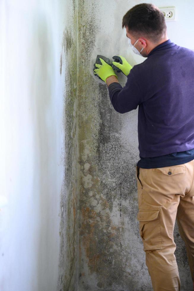 o homem usa uma espátula para remover mofo e fungos na parede. foto