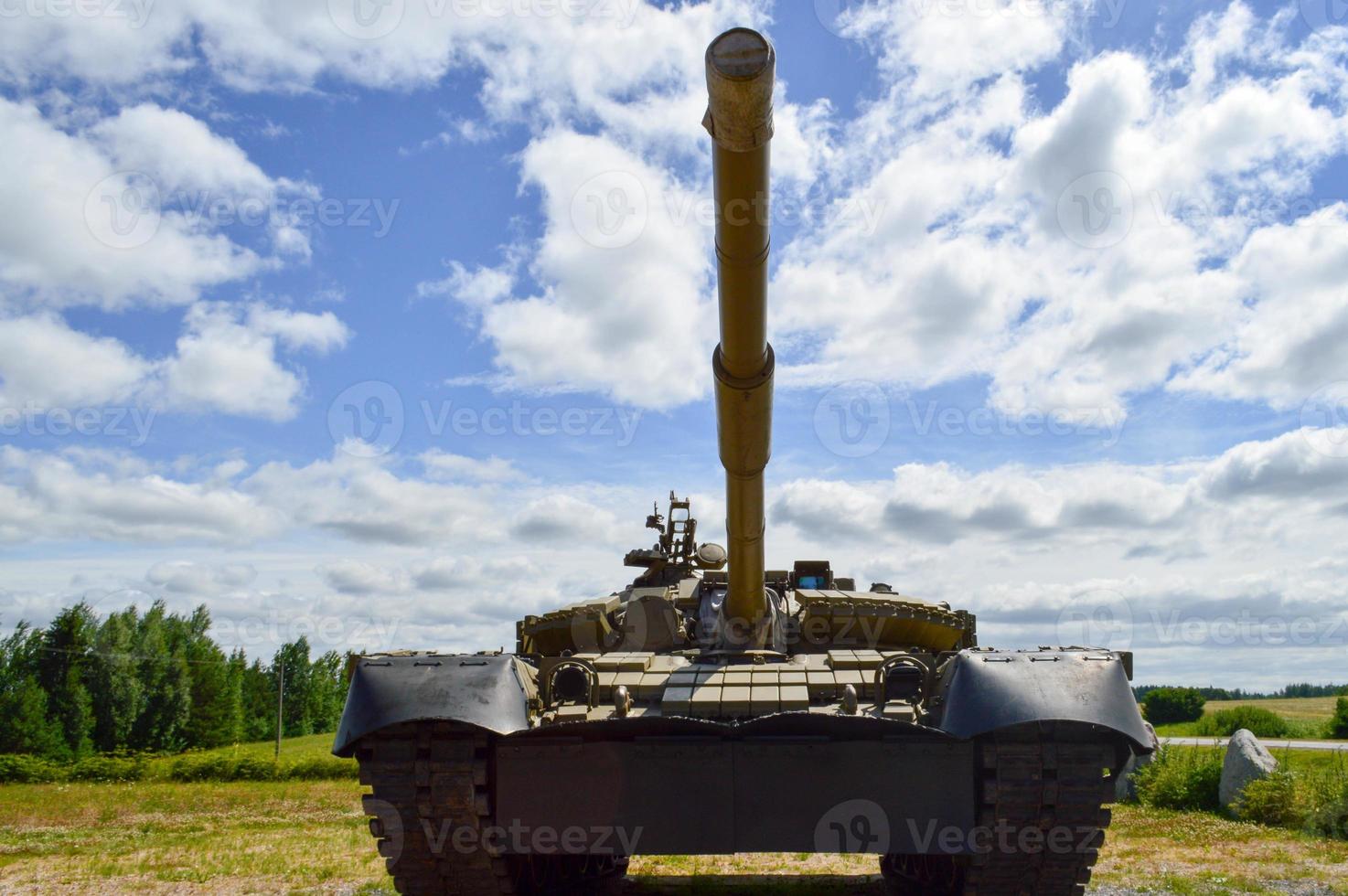 um grande metal militar verde blindado mortalmente perigoso tanque de batalha sírio russo com uma torre de canhão e um ganso está estacionado contra um céu azul e nuvens fora da cidade foto