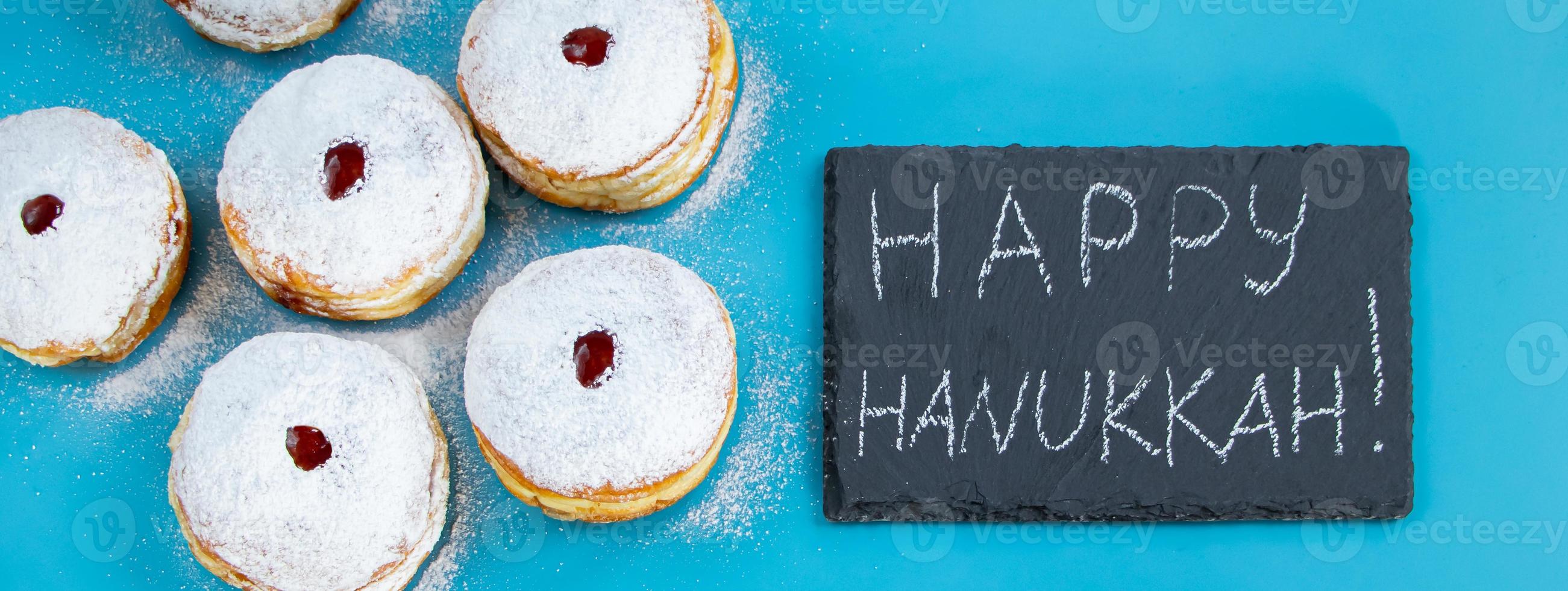 Feliz Hanukkah. rosquinhas sufganiyot de sobremesa judaica sobre fundo azul. símbolo do feriado religioso do judaísmo. inscrição no quadro de giz. foto