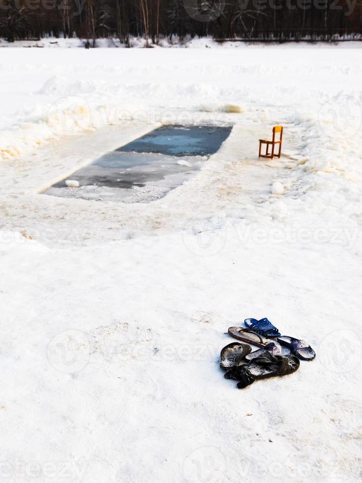 chinelos e cadeira perto do buraco no gelo no lago congelado foto