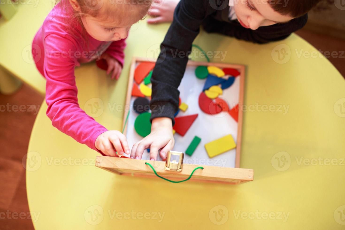 as crianças jogam jogos educativos magnéticos de madeira juntos. vista de cima. as crianças brincam com um construtor foto