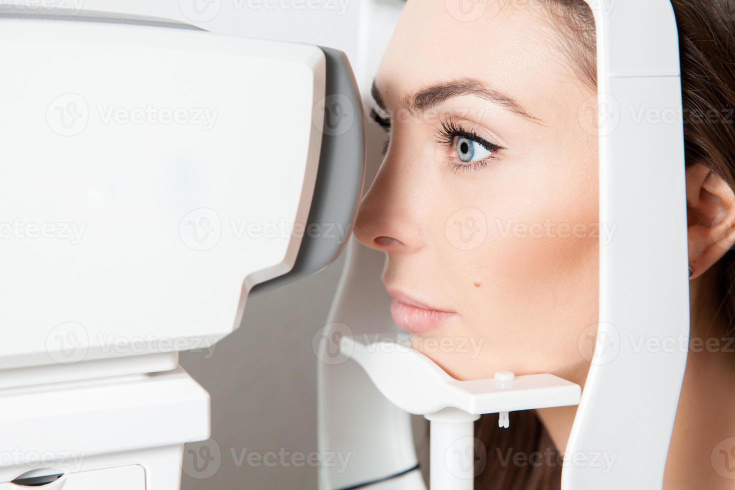 doce jovem morena adulta olhando para a máquina de teste ocular no oftalmologista foto