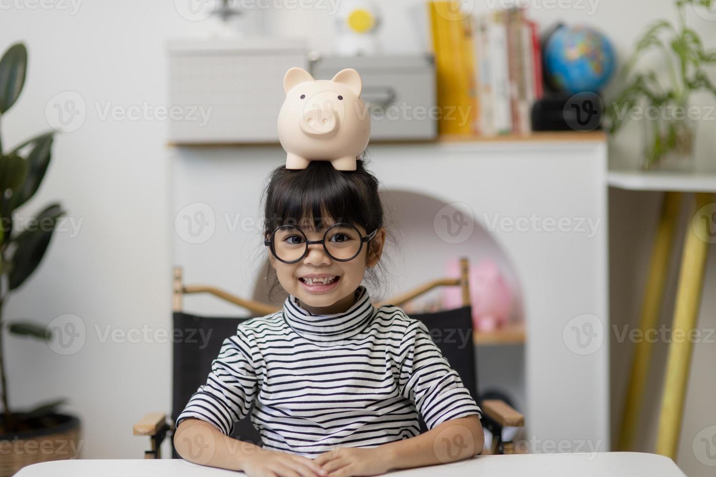 menina bonita criança asiática colocando dinheiro no cofrinho para economizar dinheiro para o futuro foto