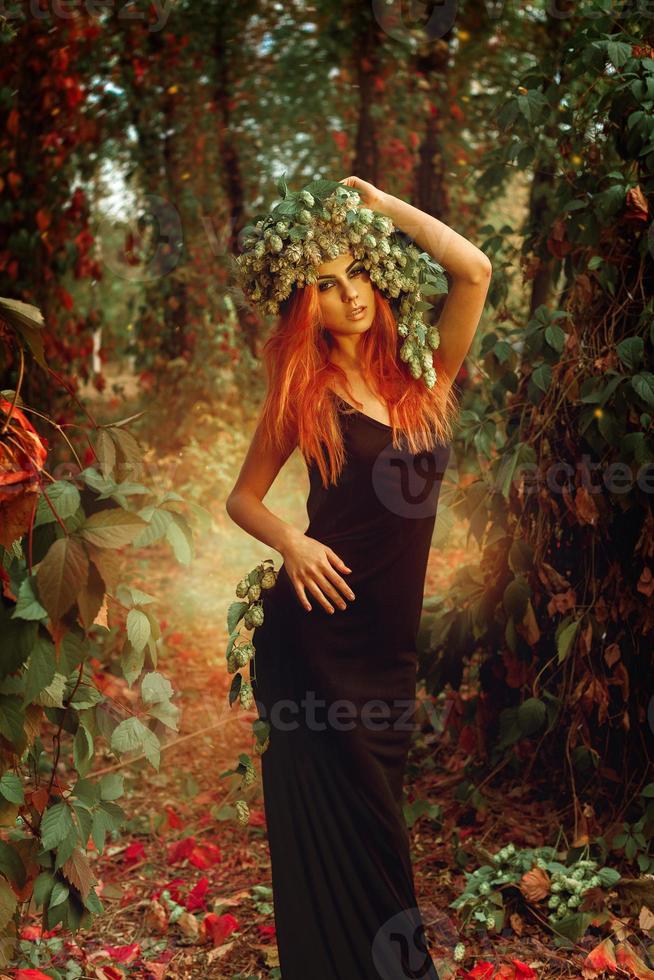 senhora ruiva de glamour com coroa de lúpulo na floresta mágica foto