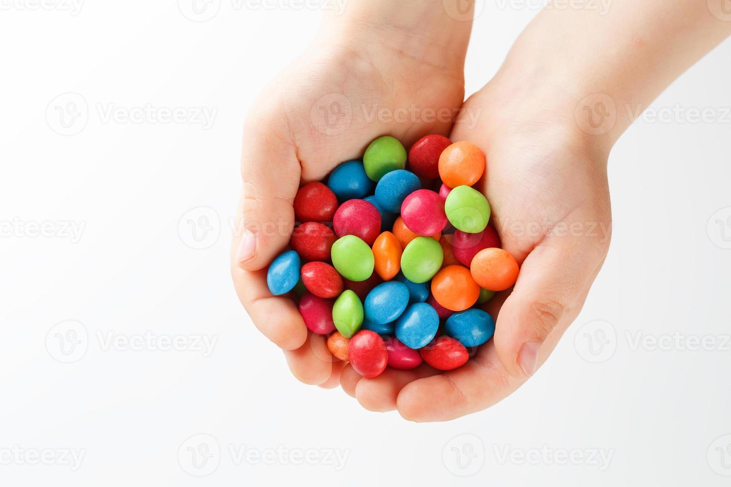 doces multicoloridos nas mãos de uma criança em um fundo branco e isolado foto
