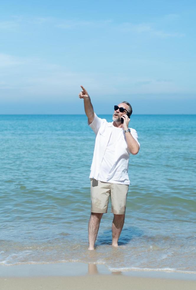 turistas estrangeiros passeiam pelas belas praias de mar azul da ásia. falando ao telefone com um amigo para descrever a beleza da praia foto