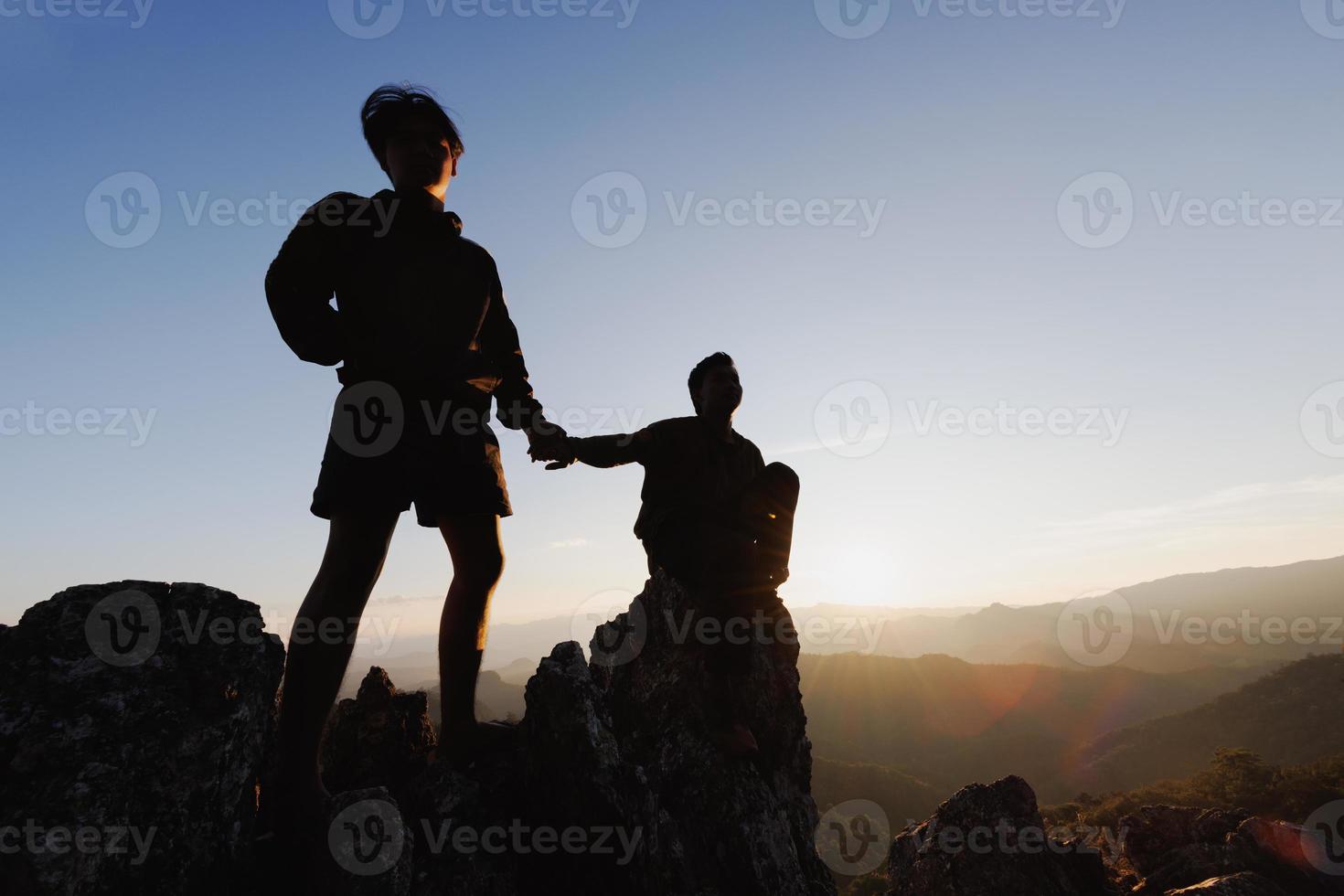 silhueta de alpinista ajudando uns aos outros a subir uma montanha ao pôr do sol. pessoas ajudando e, conceito de trabalho em equipe. foto