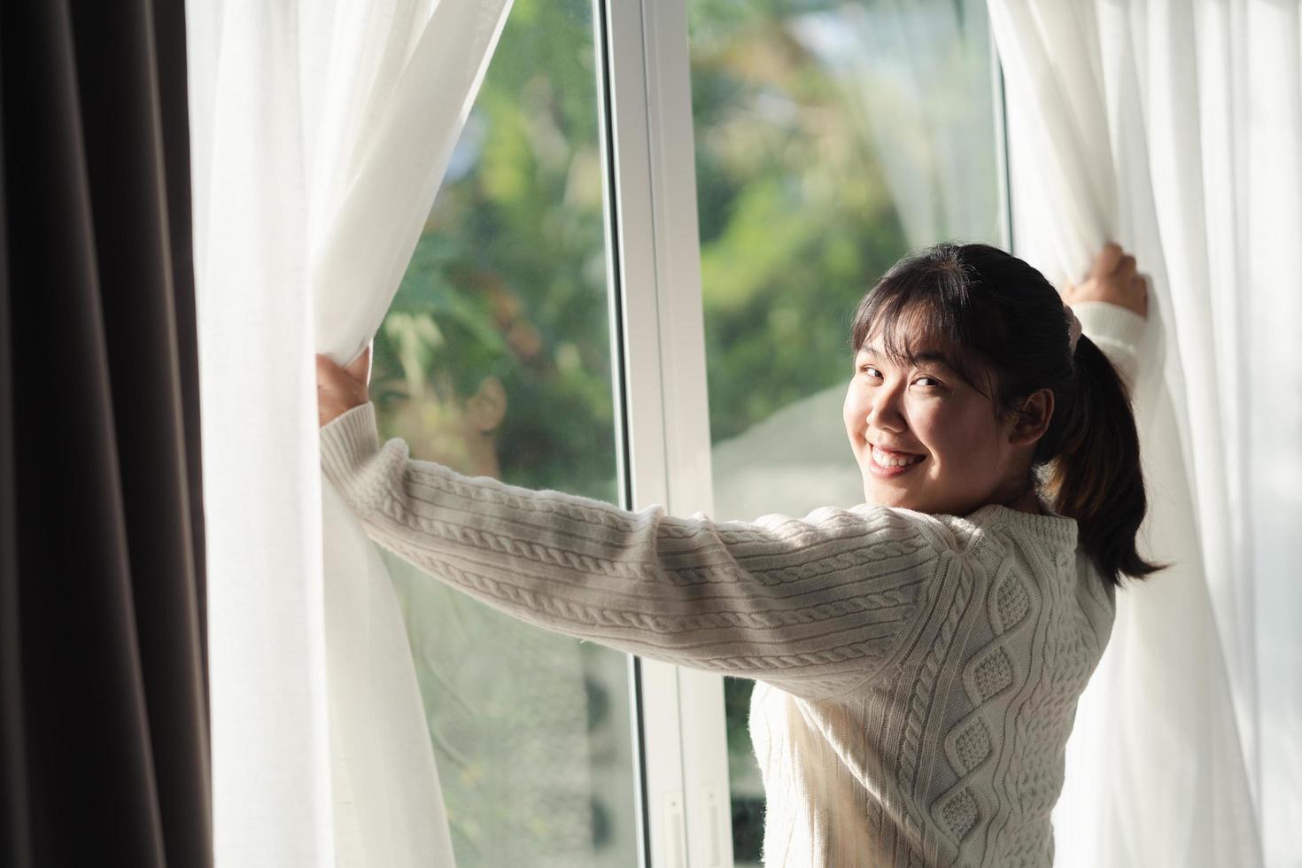 mulher feliz abrindo as cortinas da janela pela manhã. foto