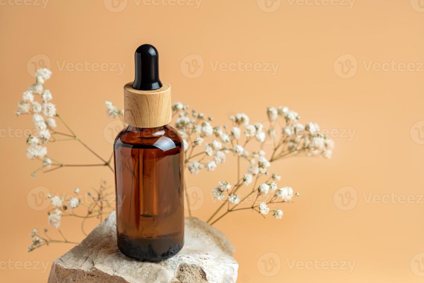 conceito estético minimalista de cuidados de beleza. frasco de cosméticos de óleo de soro orgânico feito de vidro escuro em pedra com flores contra fundo bege neutro. pele corporal, composição de produtos de tratamento facial. foto