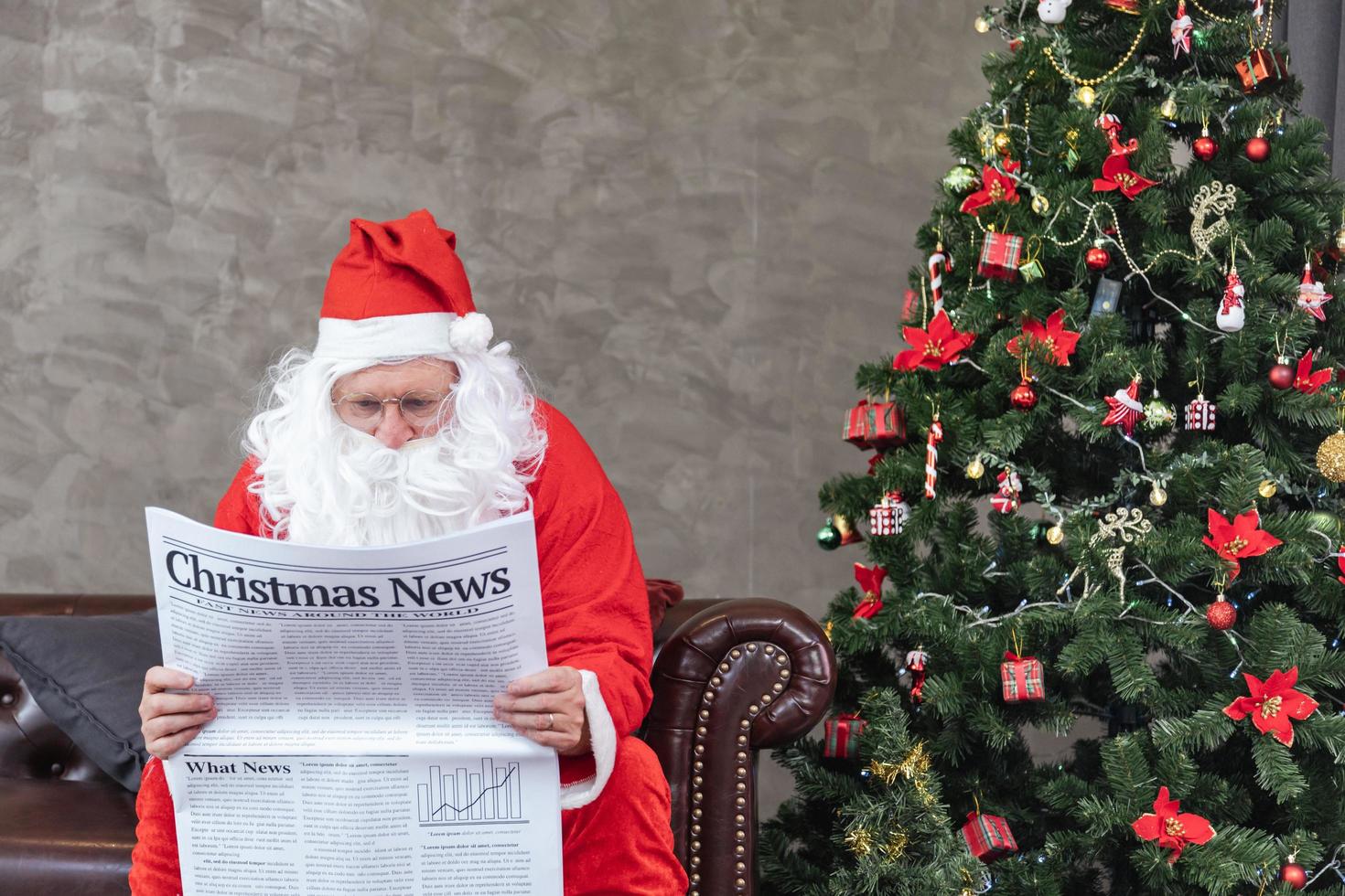 papai noel está lendo notícias de natal do jornal enquanto está sentado no sofá sofá perto da árvore de natal para situação econômica de férias longas e relatório de transporte de tráfego de acidentes foto