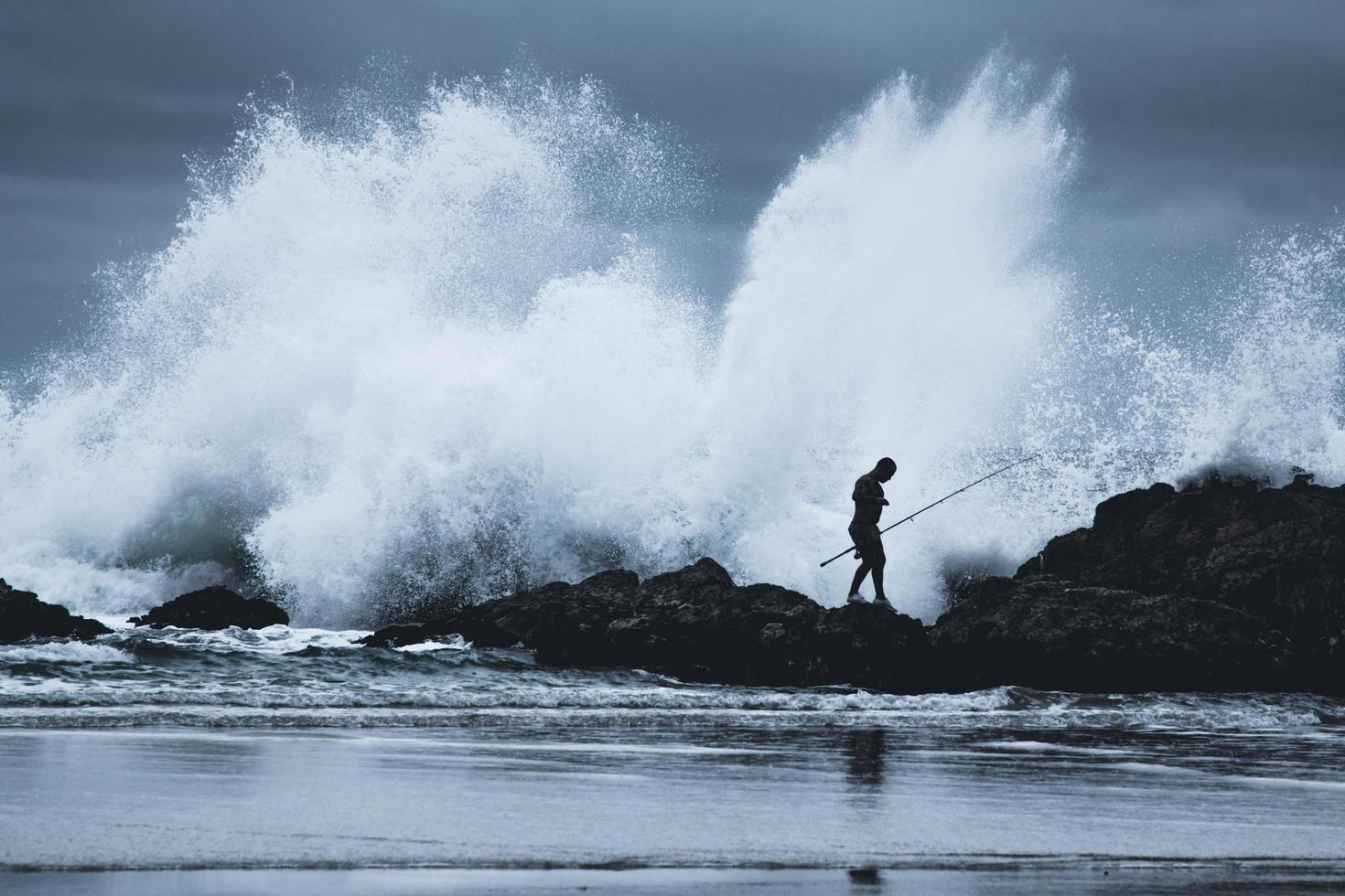 sydney, austrália, 2020 - silhueta de um homem com vara de pescar caminhando em uma costa rochosa foto