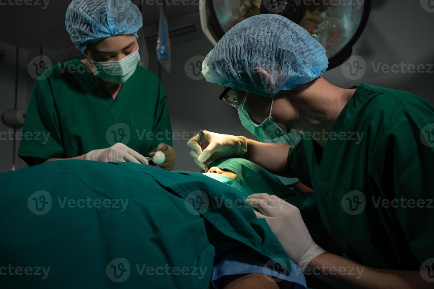 equipe de cirurgiões profissionais asiáticos realizando cirurgia na sala de cirurgia, cirurgião, assistentes e enfermeiras realizando cirurgia em um paciente, câncer de saúde e conceito de tratamento de doenças foto