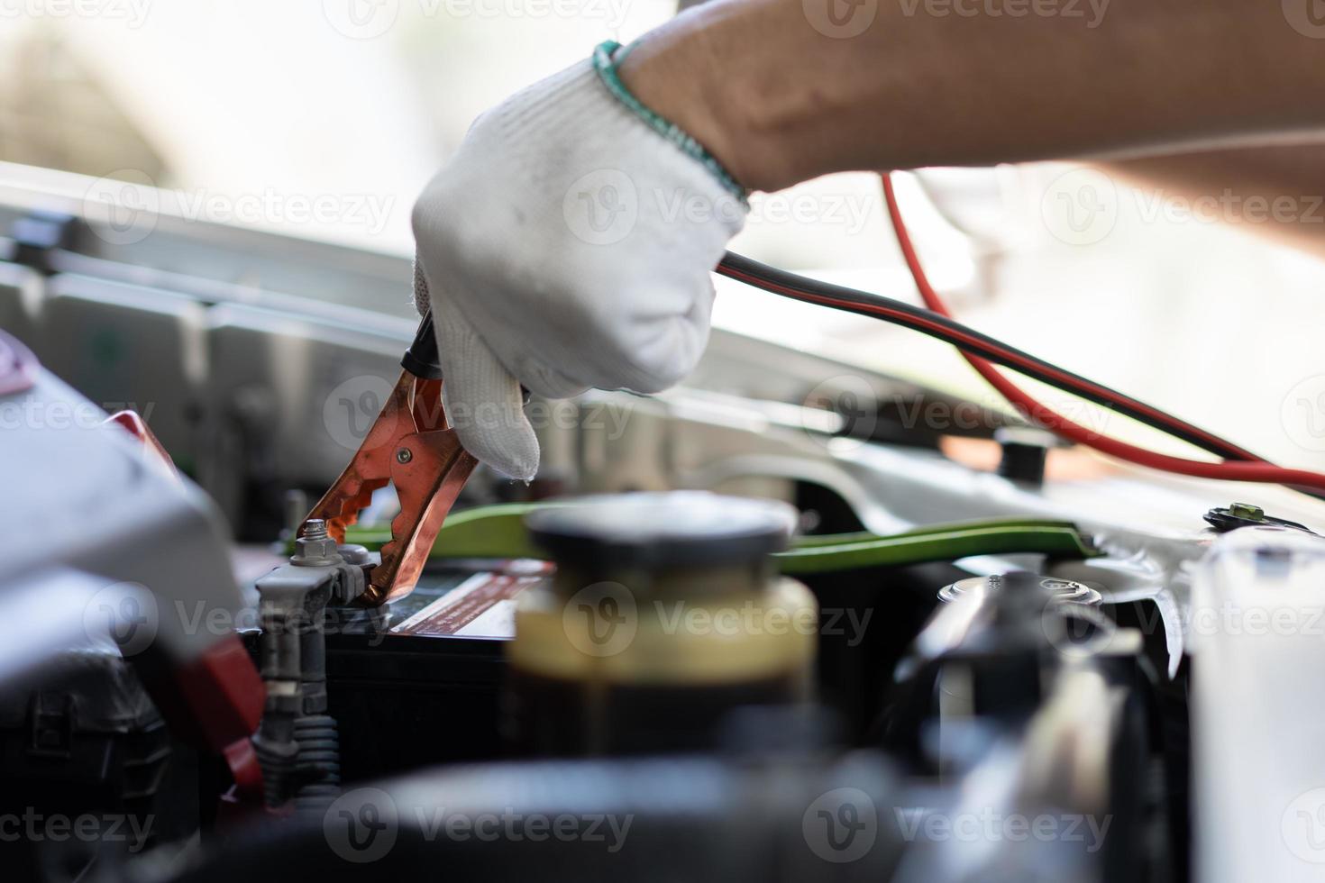 close-up e foco seletivo do mecânico de automóveis segurando o jumper de cabos de eletricidade da bateria para carregar a bateria do carro, conceito de máquina de motor de carro de serviços foto