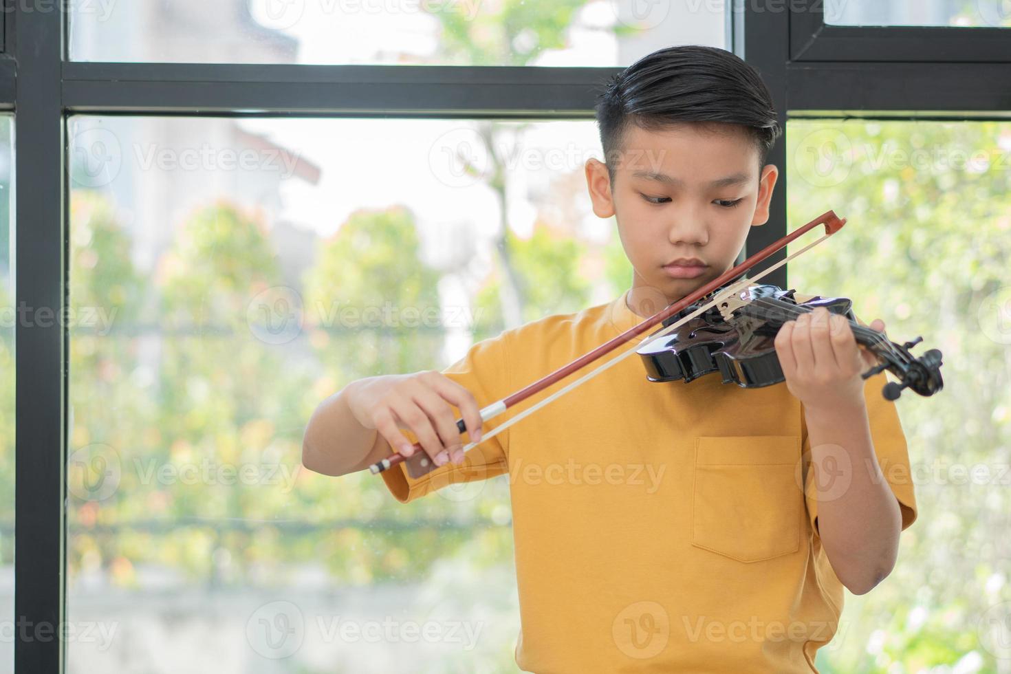 uma criança asiática tocando e praticando violino instrumento musical de cordas contra em casa, conceito de educação musical, inspiração, estudante de escola de arte adolescente. foto