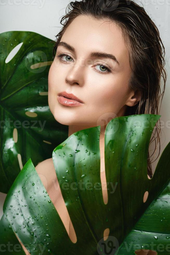 jovem mulher com uma pele lisa segurando a folha da planta monstera deliciosa foto