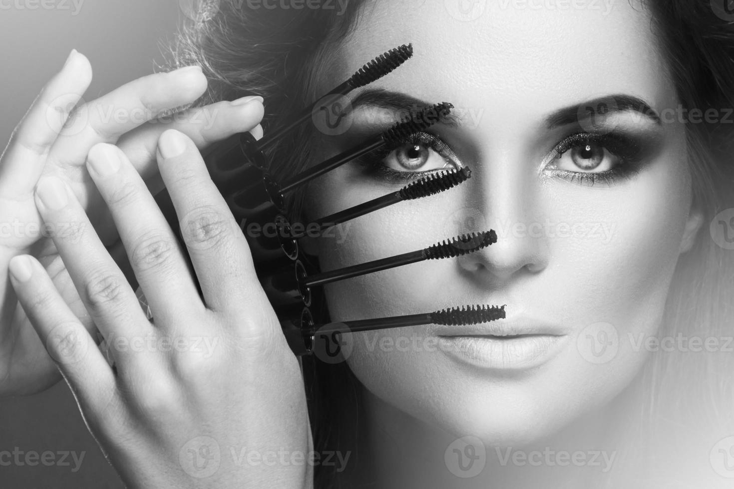 mulher deslumbrante com maquiagem linda segurando muitos bastões de rímel perto do rosto foto