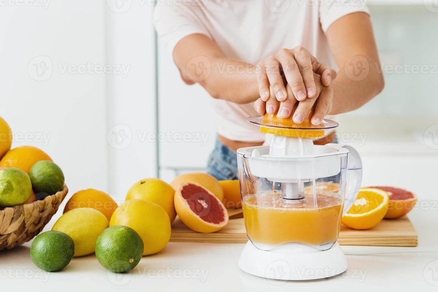 mãos femininas e espremedor de frutas cítricas durante a preparação do suco de laranja fresco foto