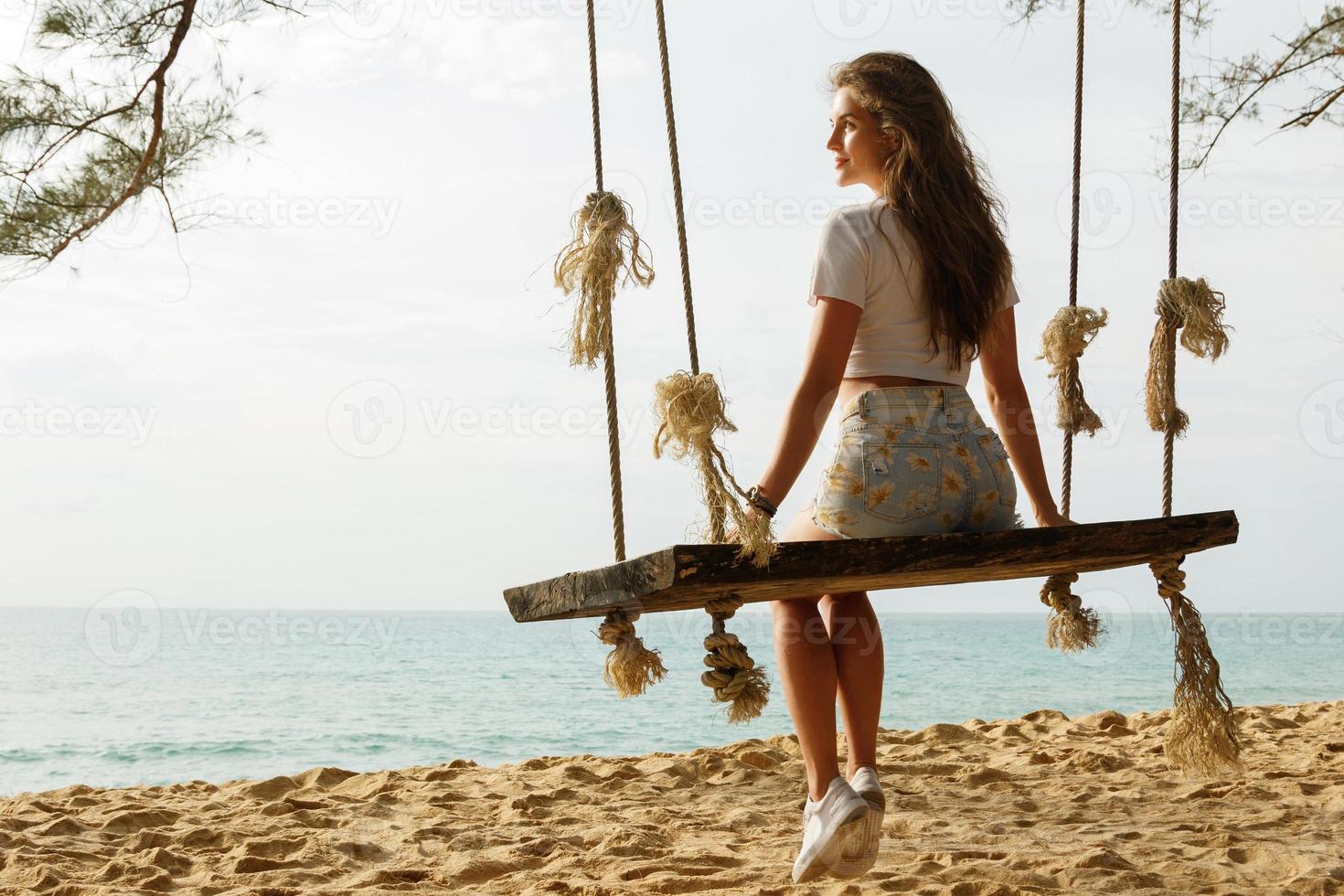 mulher vestindo shorts jeans relaxar no balanço na praia foto