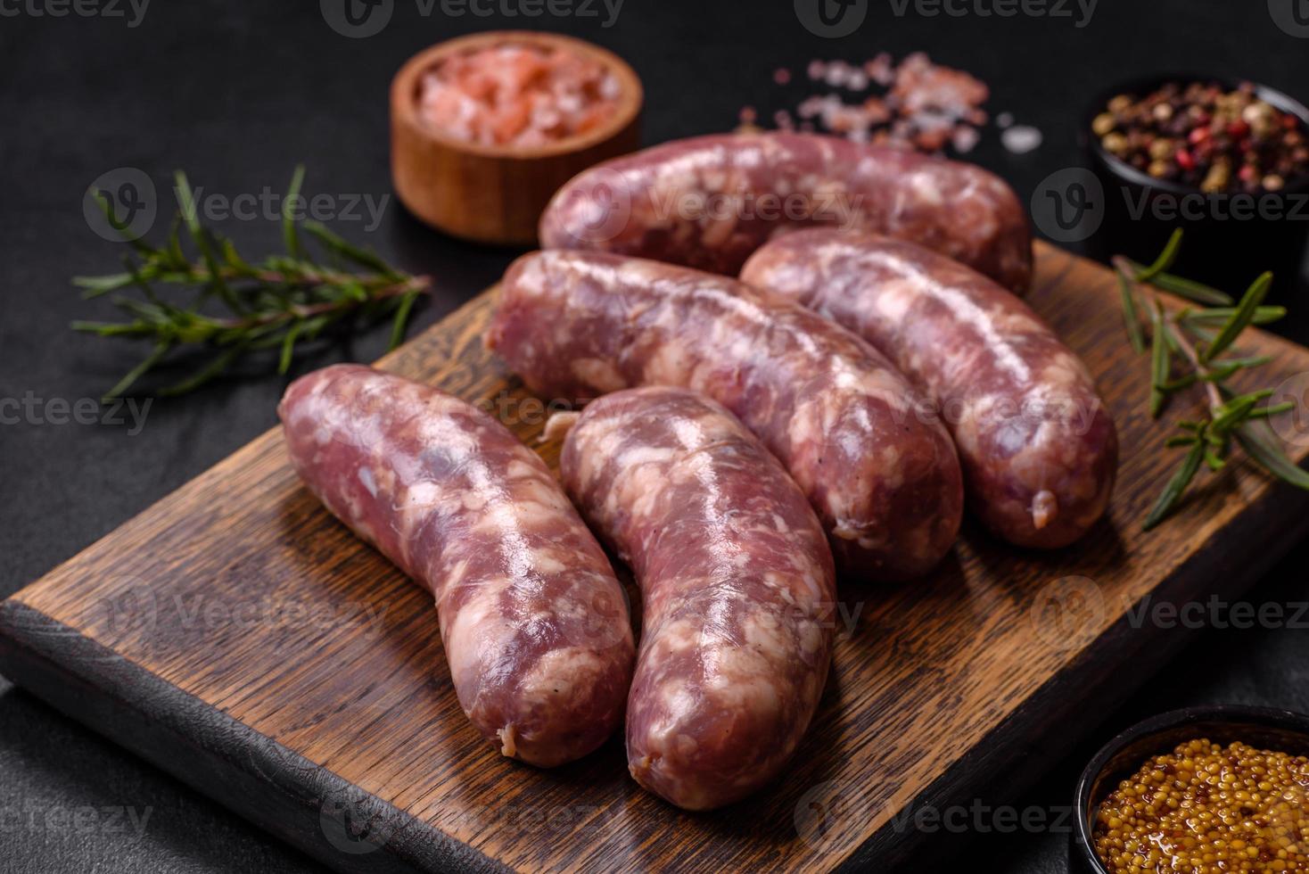 salsichas de porco cru grelhadas com especiarias e ervas em uma mesa de concreto escuro foto