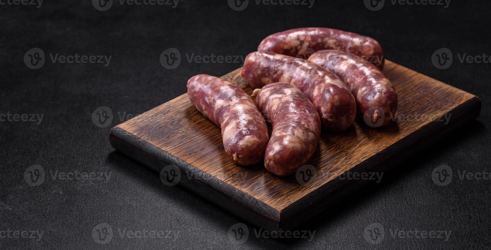 salsichas de porco cru grelhadas com especiarias e ervas em uma mesa de concreto escuro foto